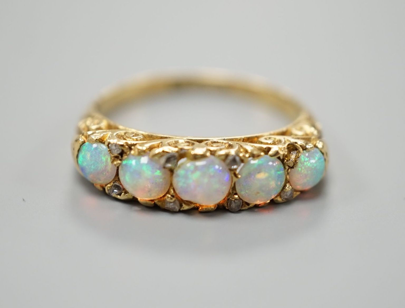 A late Victorian yellow metal and graduated five stone white opal set half hoop ring, with diamond chip spacers, size M, gross weight 3.7 grams.